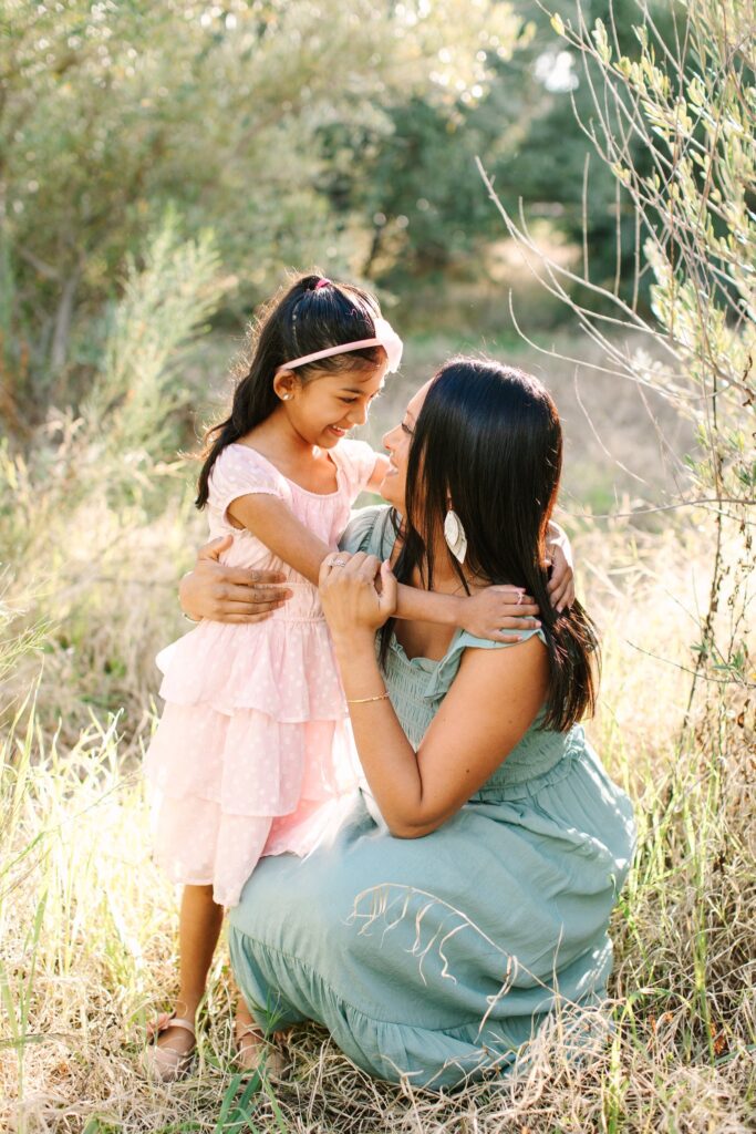 Mother and daughter in sage green and light pink dresses in an olive grove