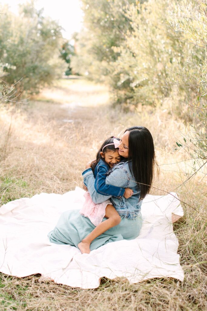 Mother and daughter hugging on a white blanket in an olive grove